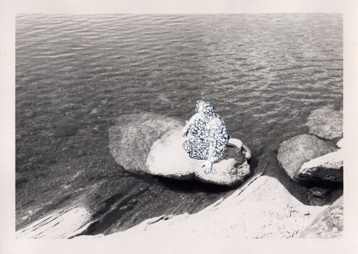 Young man seated on a rock half-submerged in water