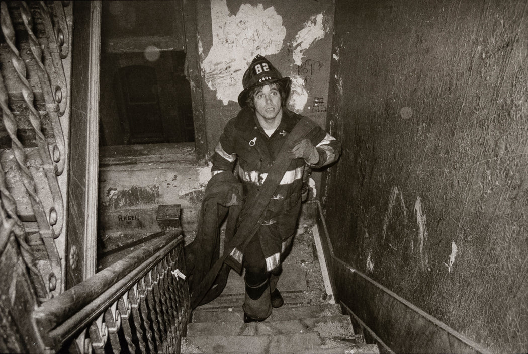 Untitled [A firefighter carries the fire hose nozzle upstairs in an apartment block in the South Bronx, New York City]