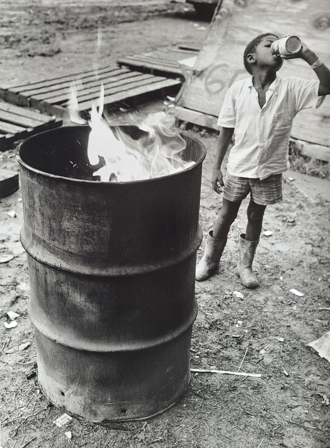 Untitled [Boy drinking next to fire in garbage can]