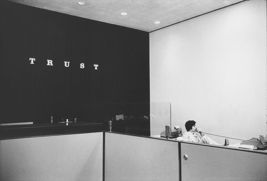 Untitled [Man on phone with “Trust” on office wall]